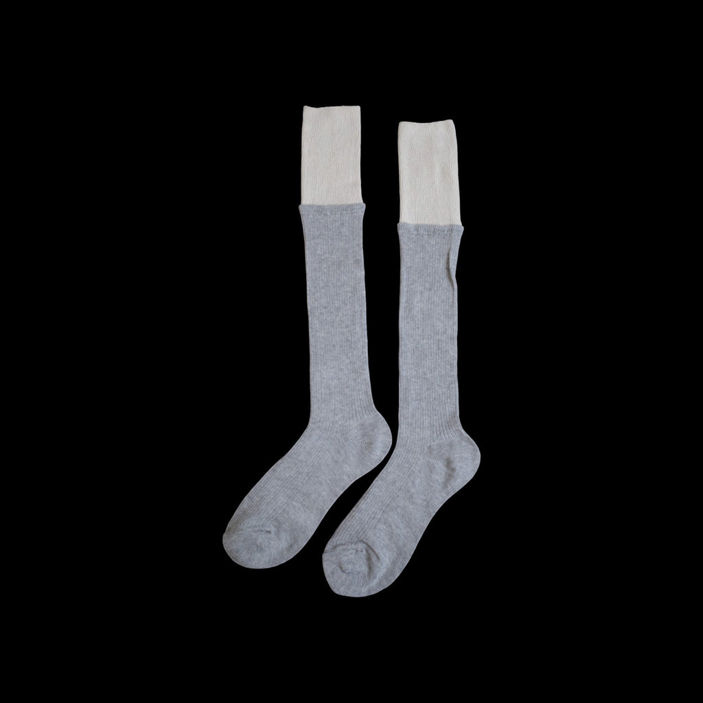 SUNMOOL grey knee-high ribbed socks with a contrasting cream dip-dyed cuff against a black background.
