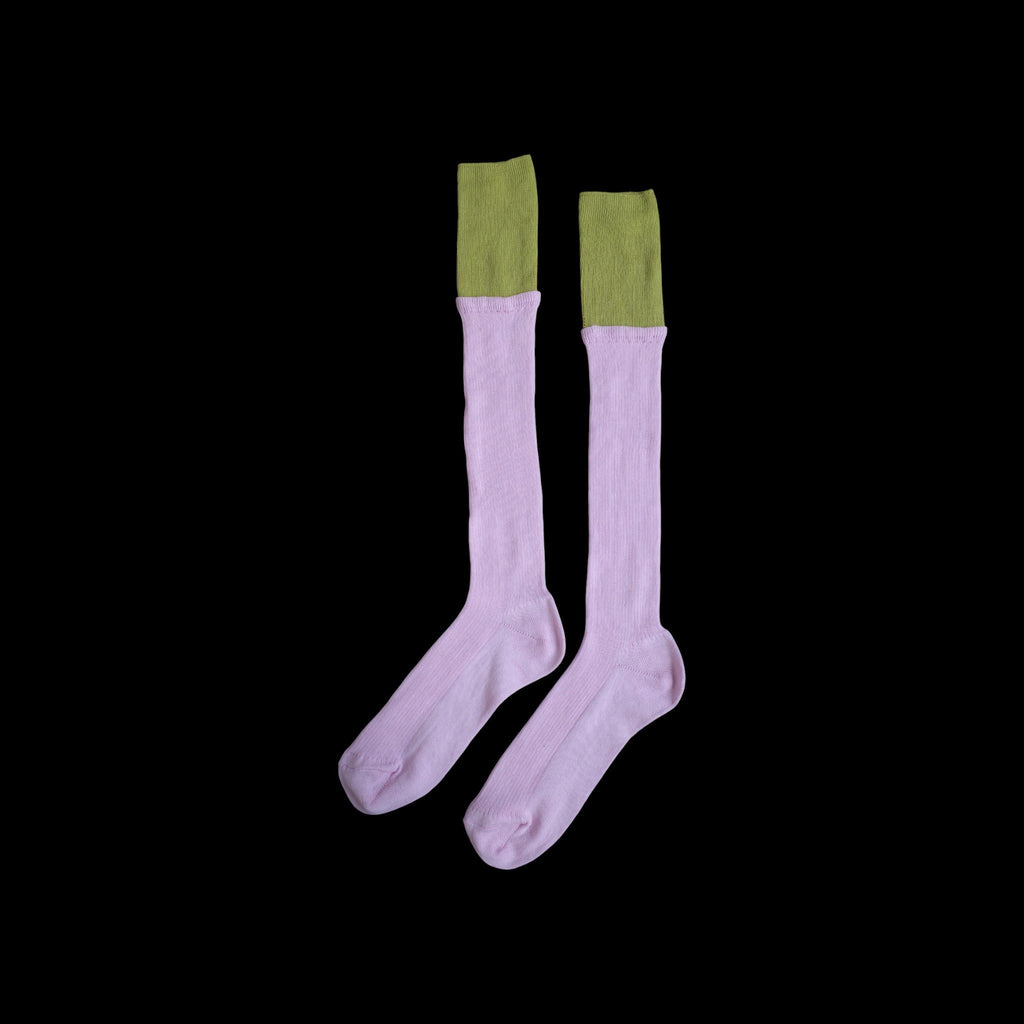 SUNMOOL knee-high ribbed socks in light pink with a contrasting olive green dip-dyed cuff against a black background.