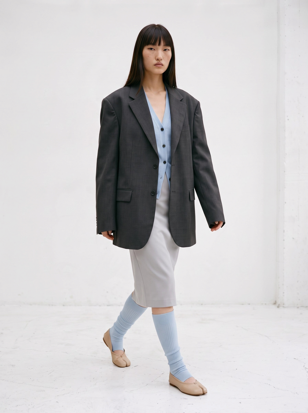 Model wearing SUNMOOL open-toe ribbed knee-high socks in light blue with beige tabi flats and a grey blazer outfit.