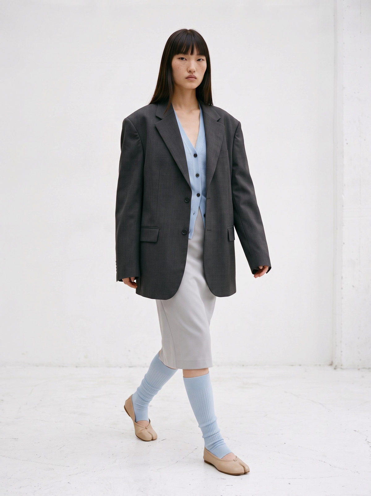 Model wearing SUNMOOL open-toe ribbed knee-high socks in light blue with beige tabi flats and a grey blazer outfit.