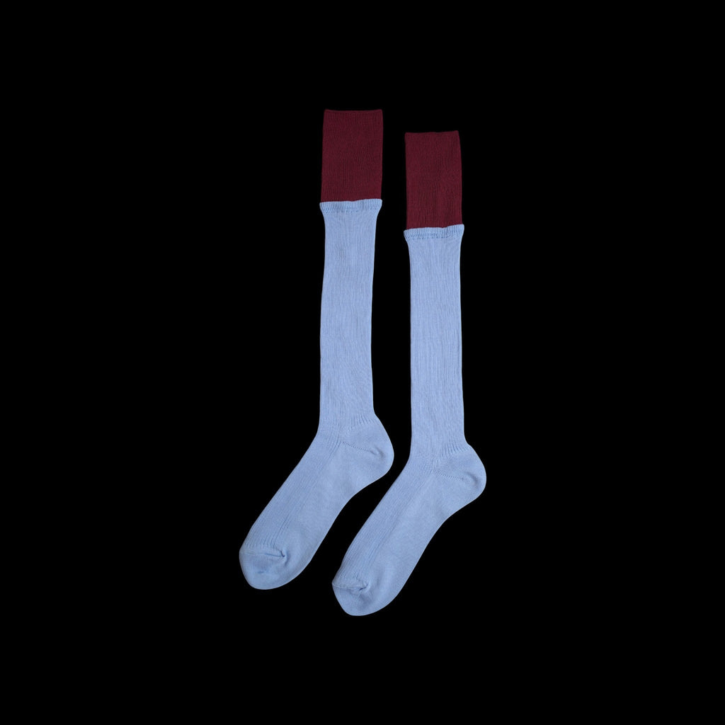 SUNMOOL sky blue knee-high socks with a contrasting dark red dip-dyed ribbed cuff on a black background.