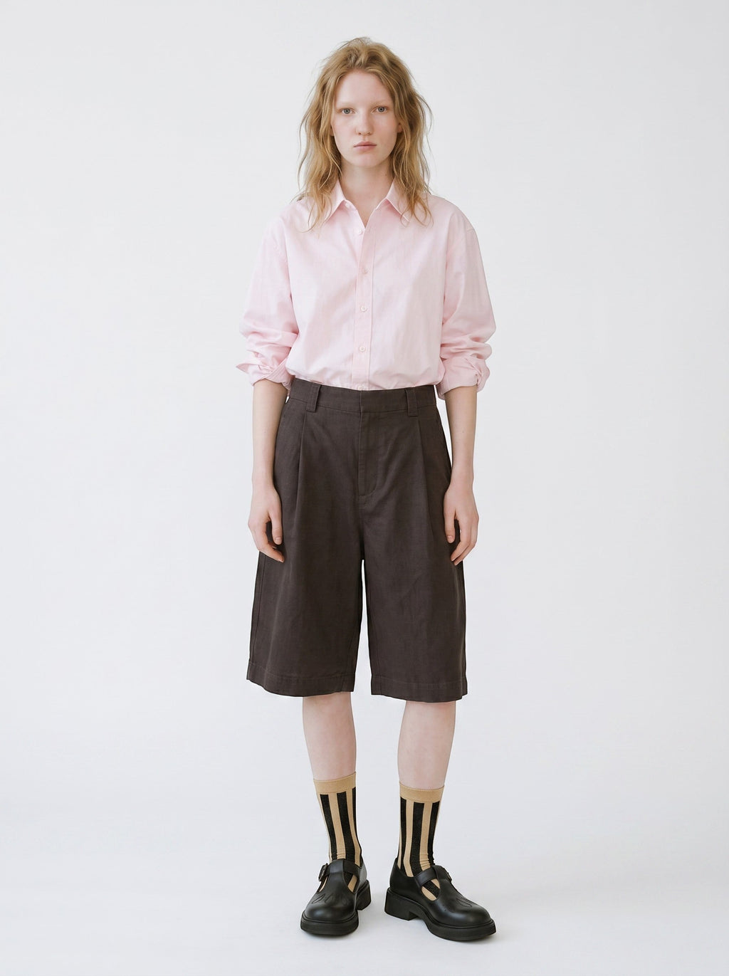 Model wearing SUNMOOL ivory and black vertical striped tinsel socks with dark shorts and black buckled shoes.